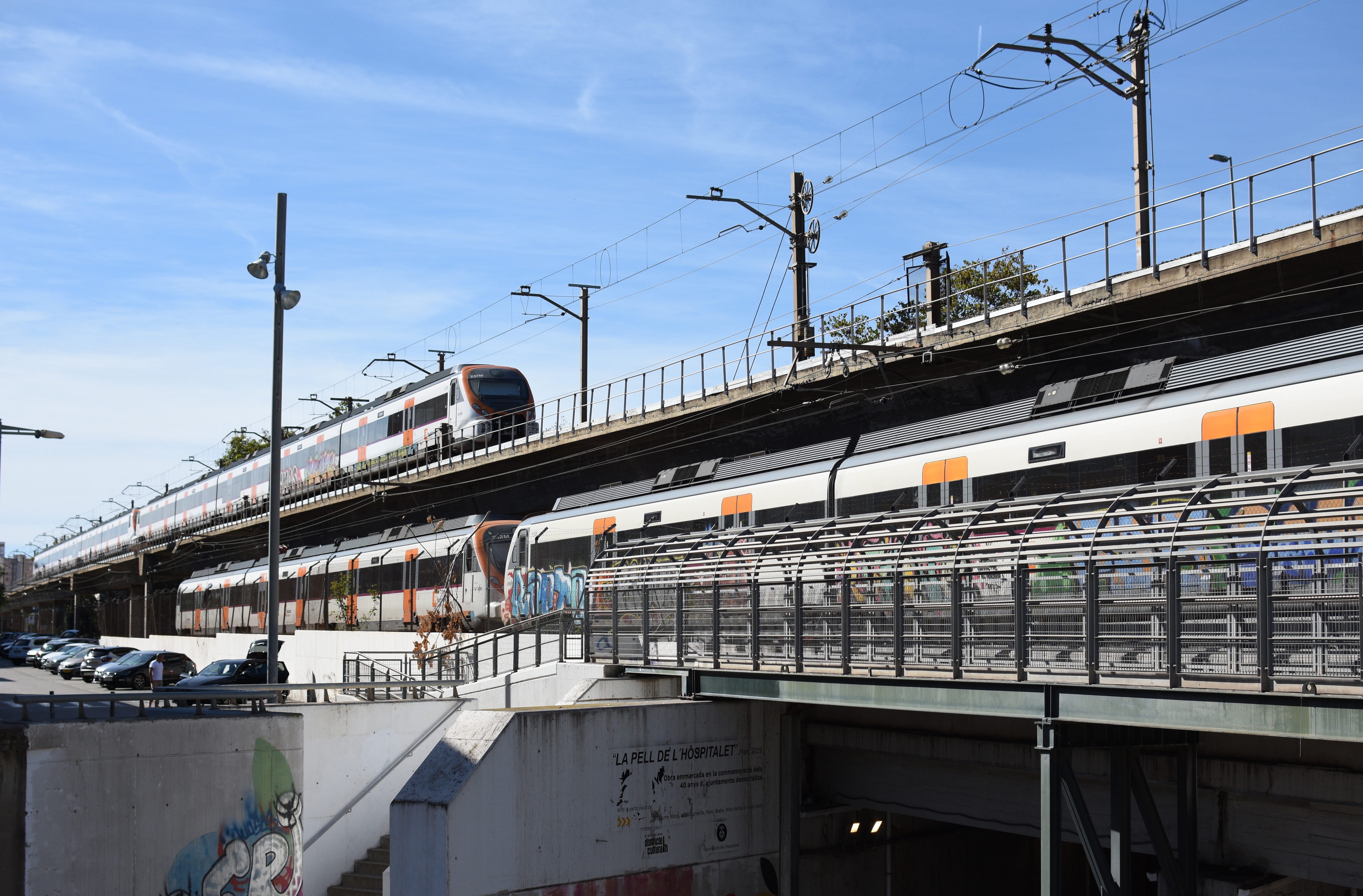 Rail bridge over a road with two trains going opposite directions. The tracks on the bridge are offset and one is elevated over the other.
